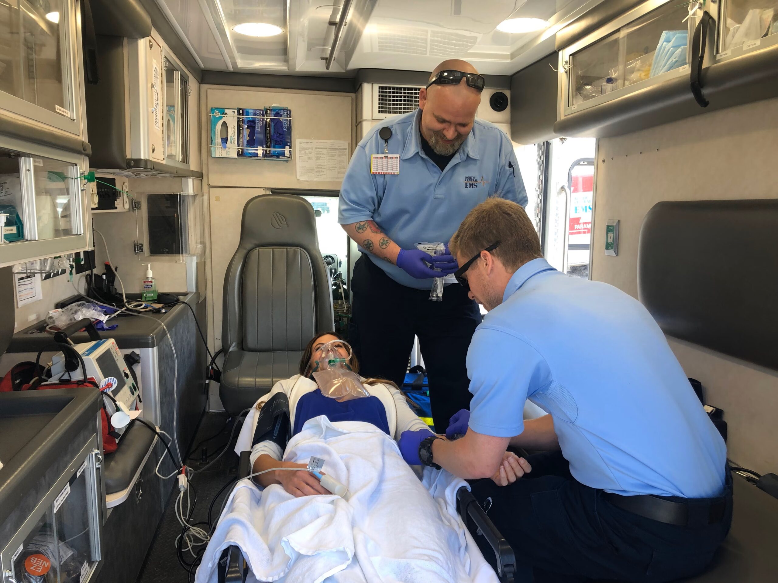 Two emergency medical service technicians helping a woman wearing an oxygen mask