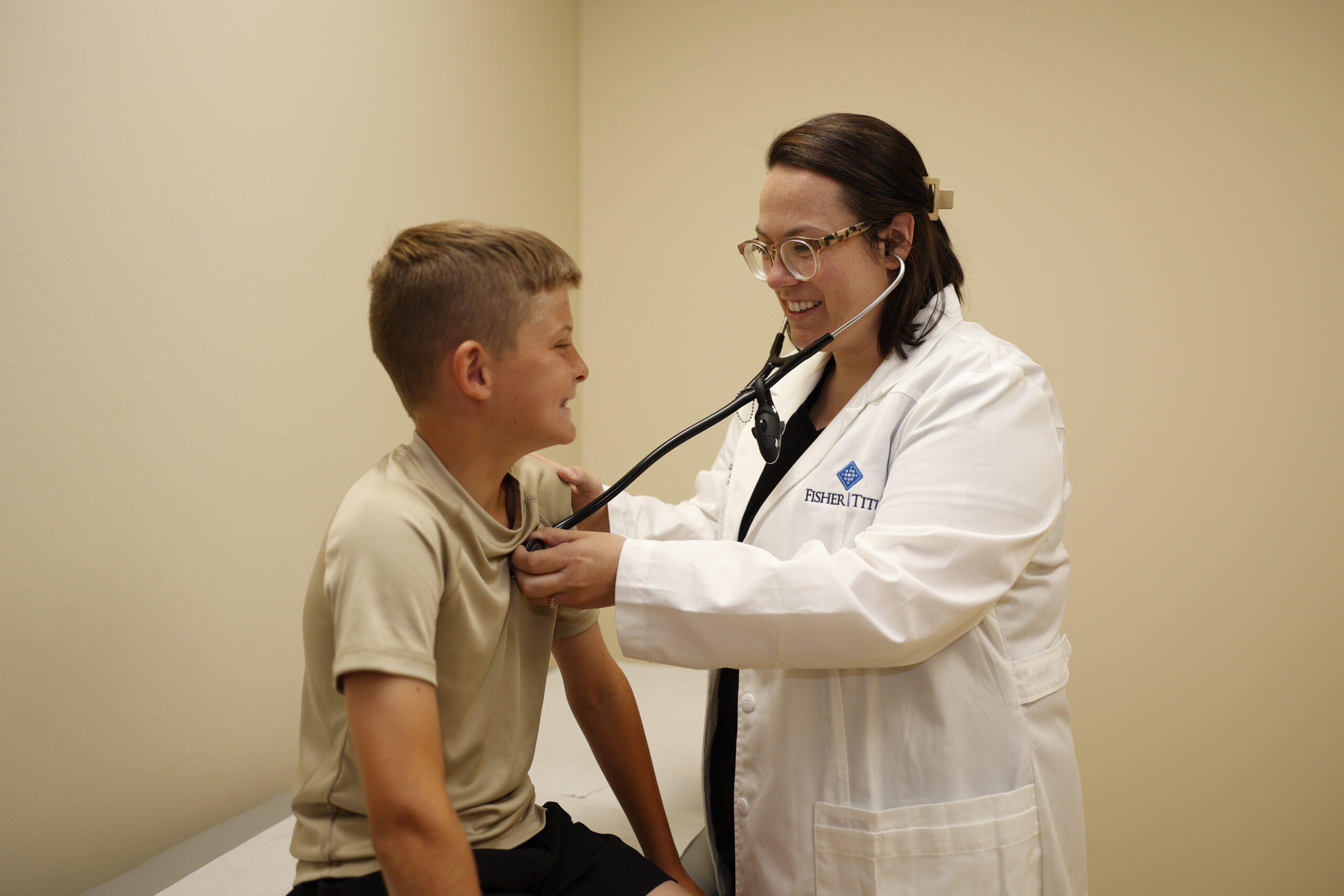 Image of a female doctor listening to a young boy's heart with a stethoscope during a physical exam.