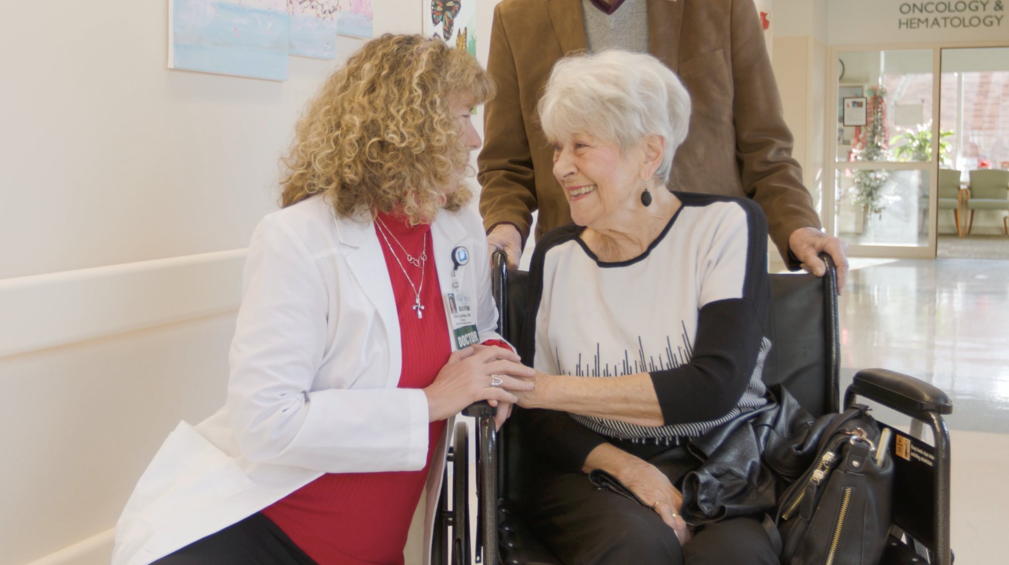 A Fisher-Titus doctor smiles and holds hands with an older woman in a wheelchair during a Medicare annual wellness visit